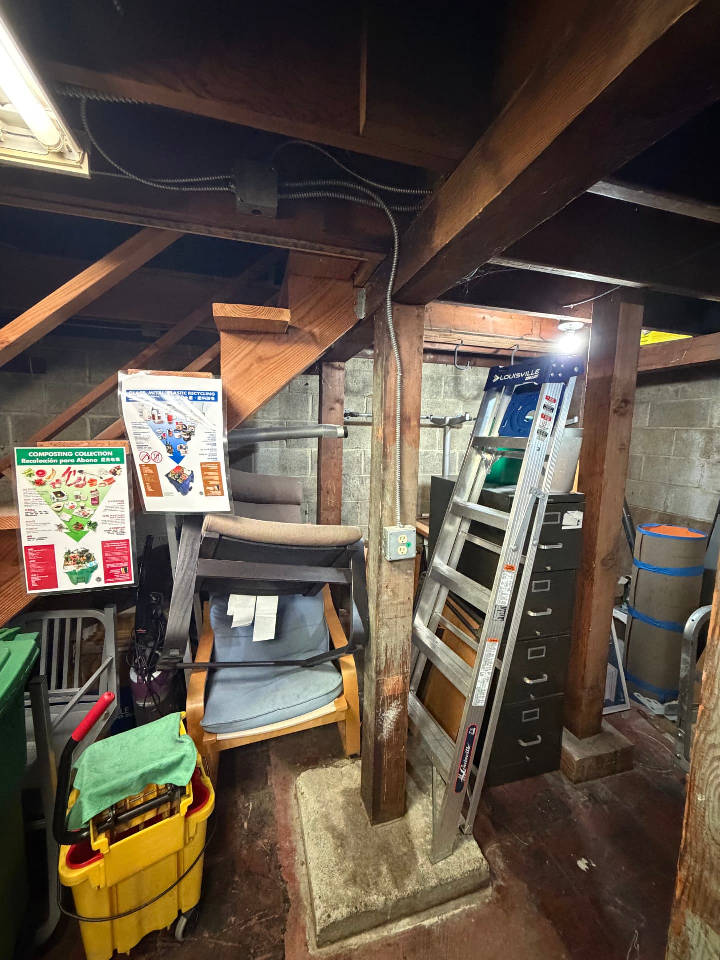 Basement cluttered with chairs, a ladder, filing cabinets and storage items before a cleanout