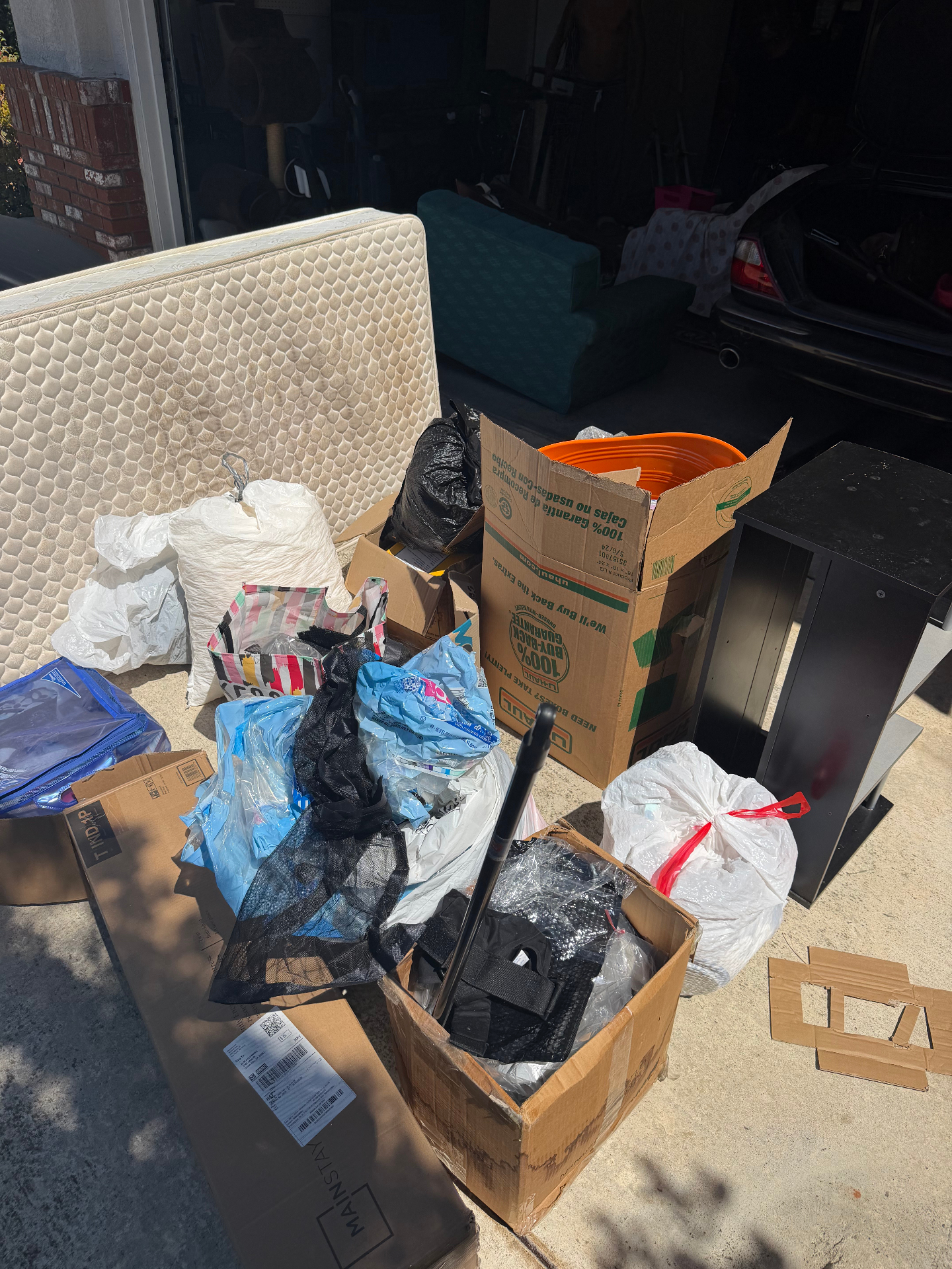 Old mattress, boxes and bagged household junk set out in a driveway for pickup